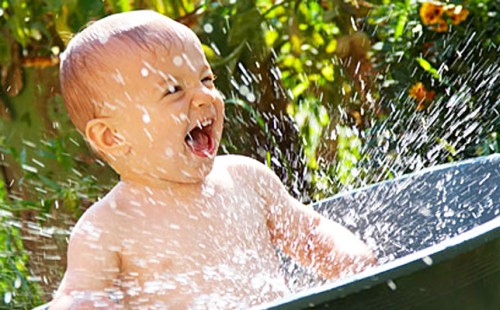 Детето щастливо вика под водния спрей